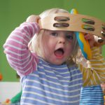 child with tambourine over their head