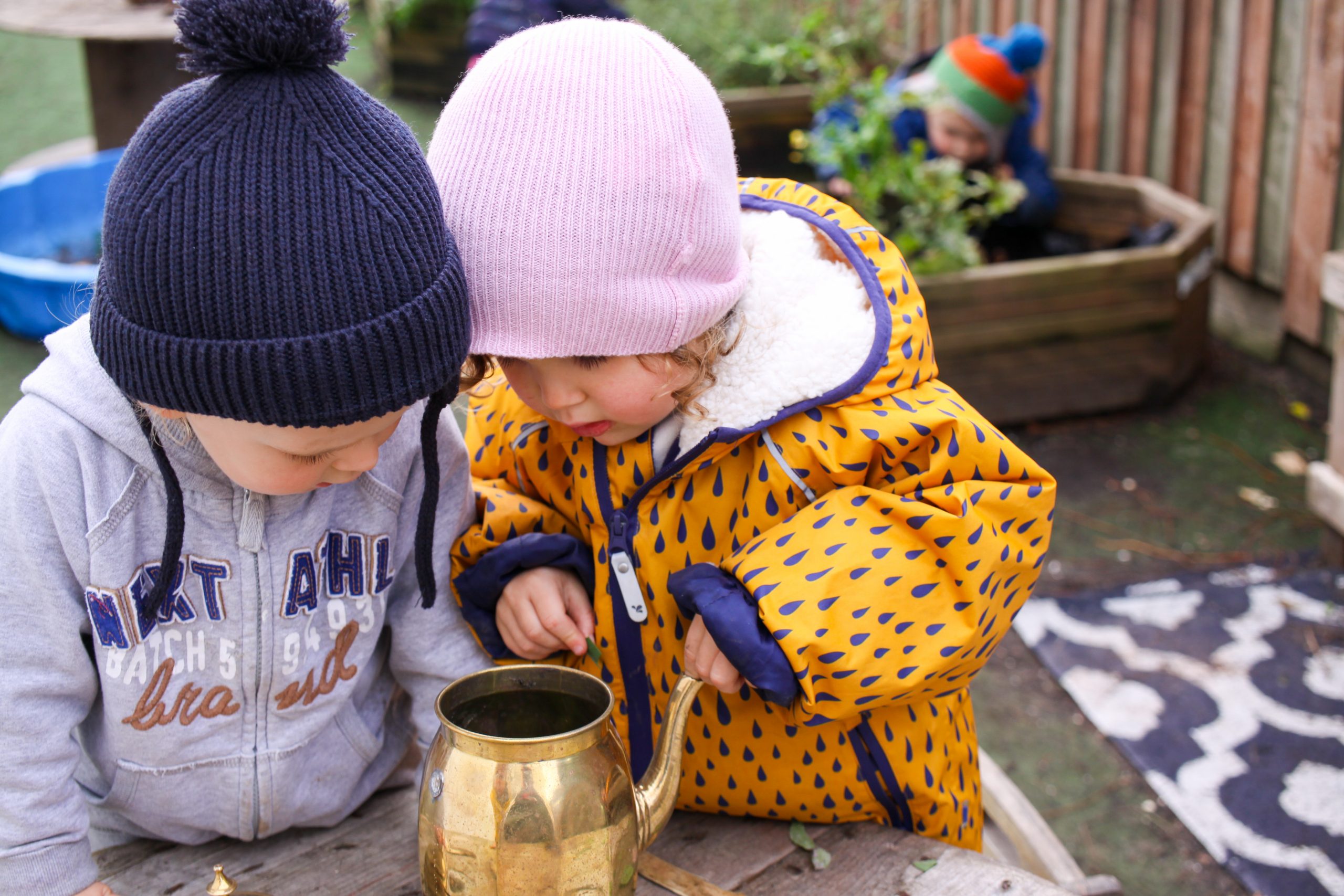 Children in garden looking into teapot