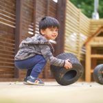 boy plays with small tyre in nursery garden