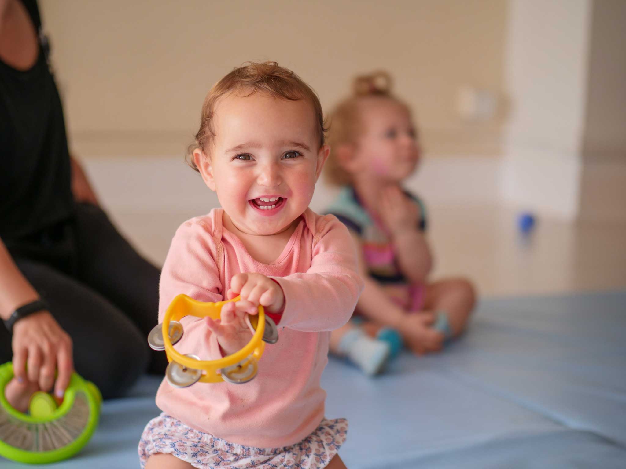 baby girl smiles at camera while holding tambourine