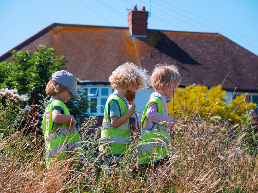 three children walking in a line through long grass