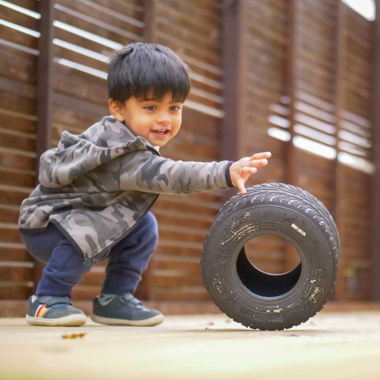 boy rolling-play tyre in nursery garden