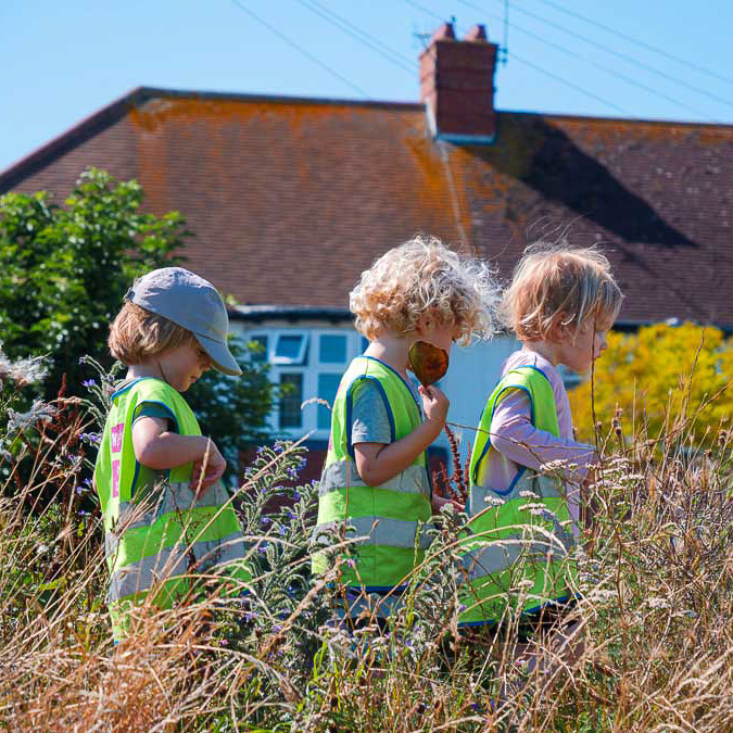 three children walking in a line through long grass