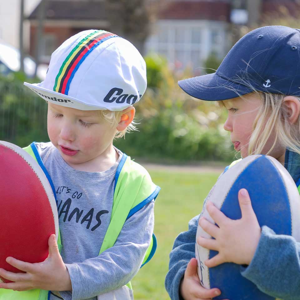 two boys looking at the rugby balls they hold
