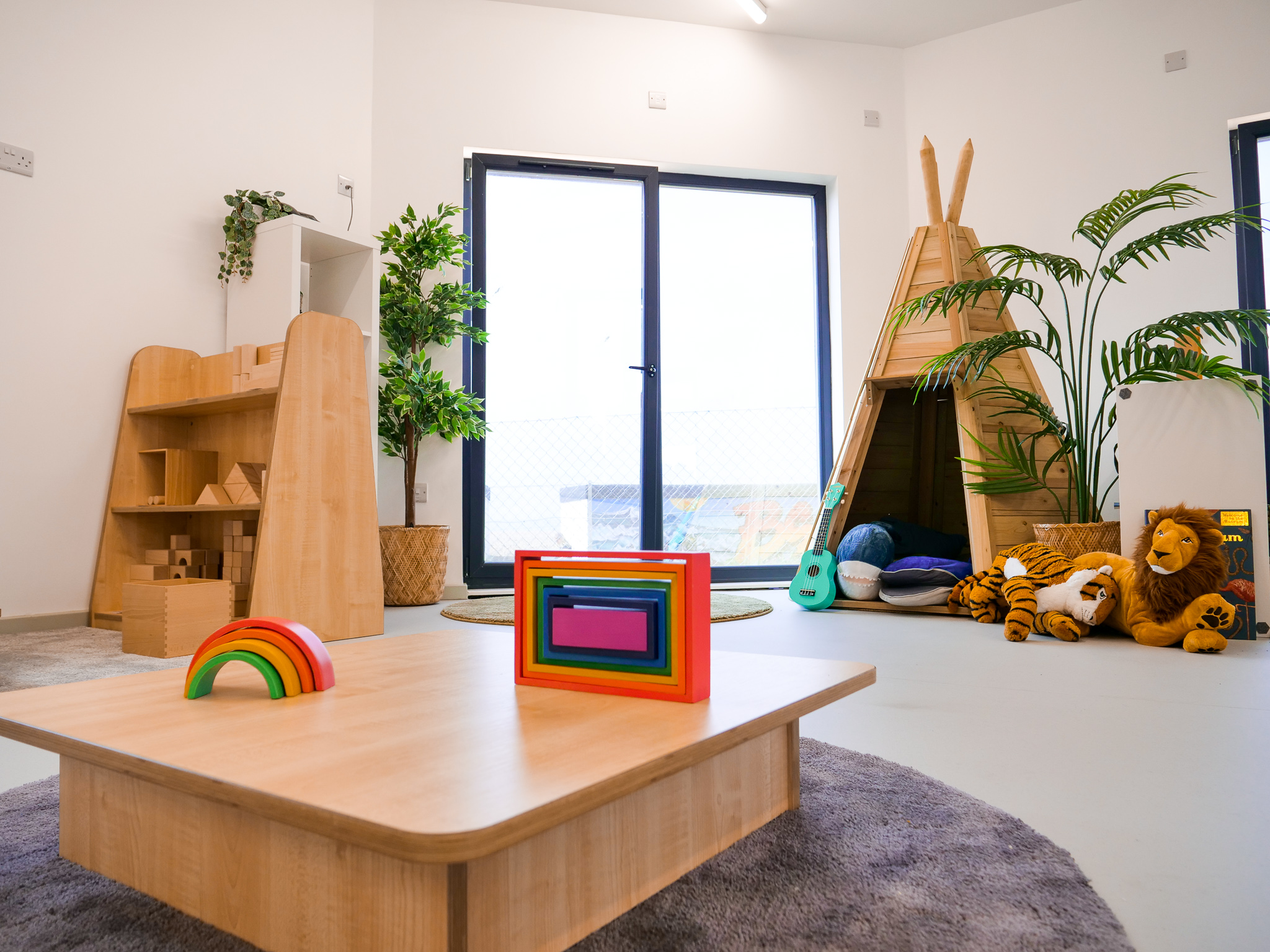 nursery interior with colourful wooden blocks, a wooden tent and cuddly animal toys